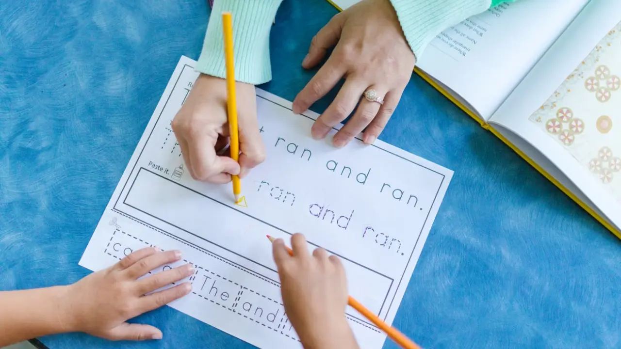 Criança praticando letras no papel com orientação de um adulto